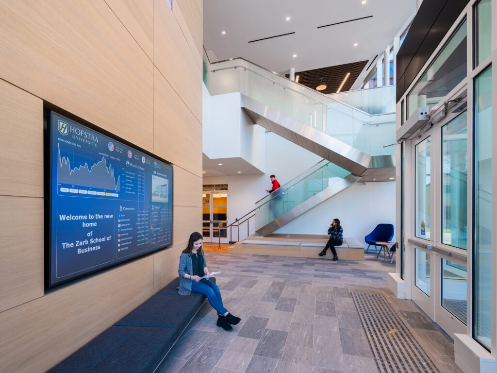 GPT
Spacious atrium of Hofstra's Zarb School of Business featuring a large digital information screen, a floating staircase with glass balustrades, and people engaged in various activities, reflecting a dynamic educational environment.