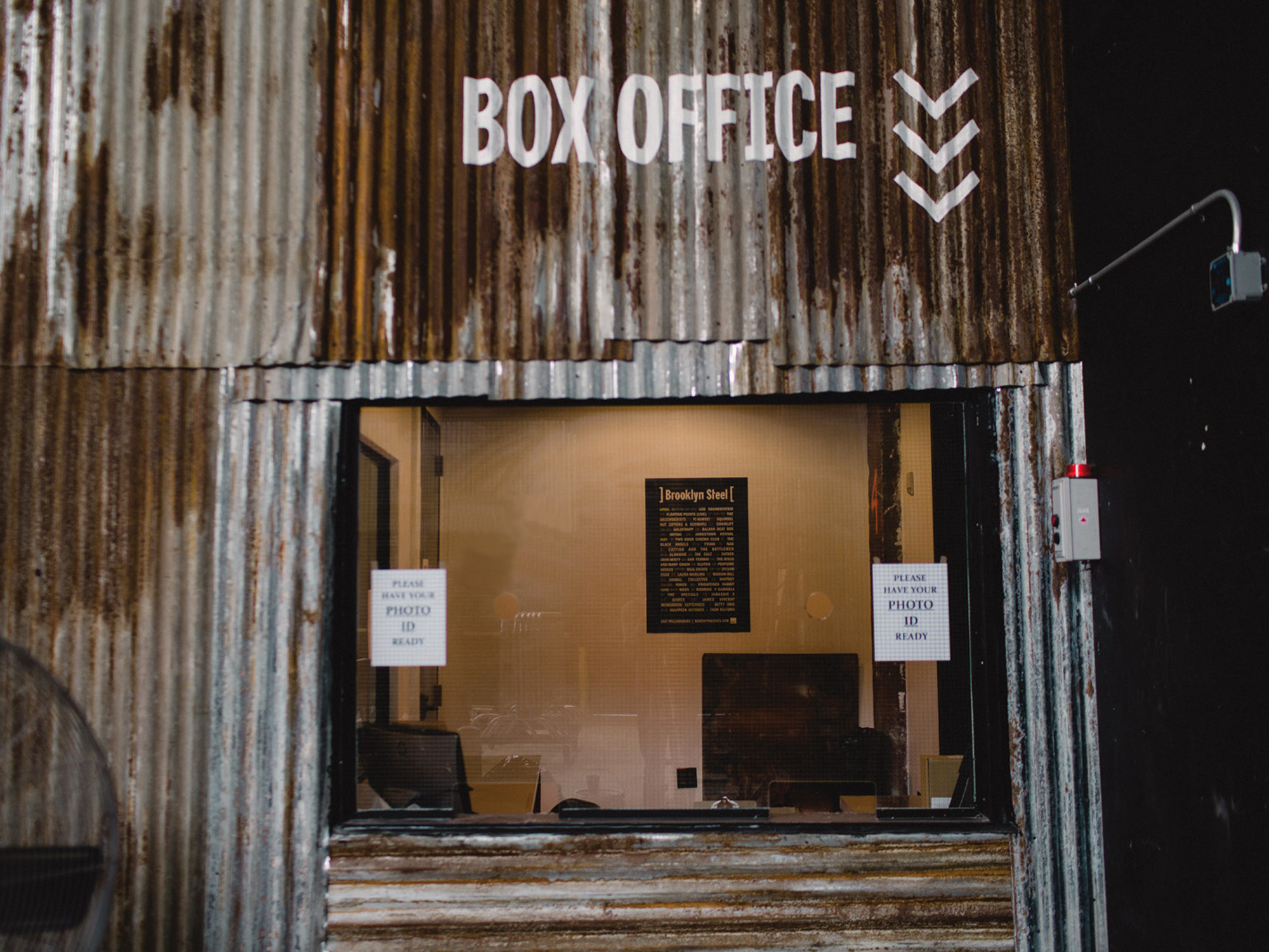 Box office window at Brooklyn Steel with a rustic corrugated metal facade and signage instructing patrons to have photo ID ready.
