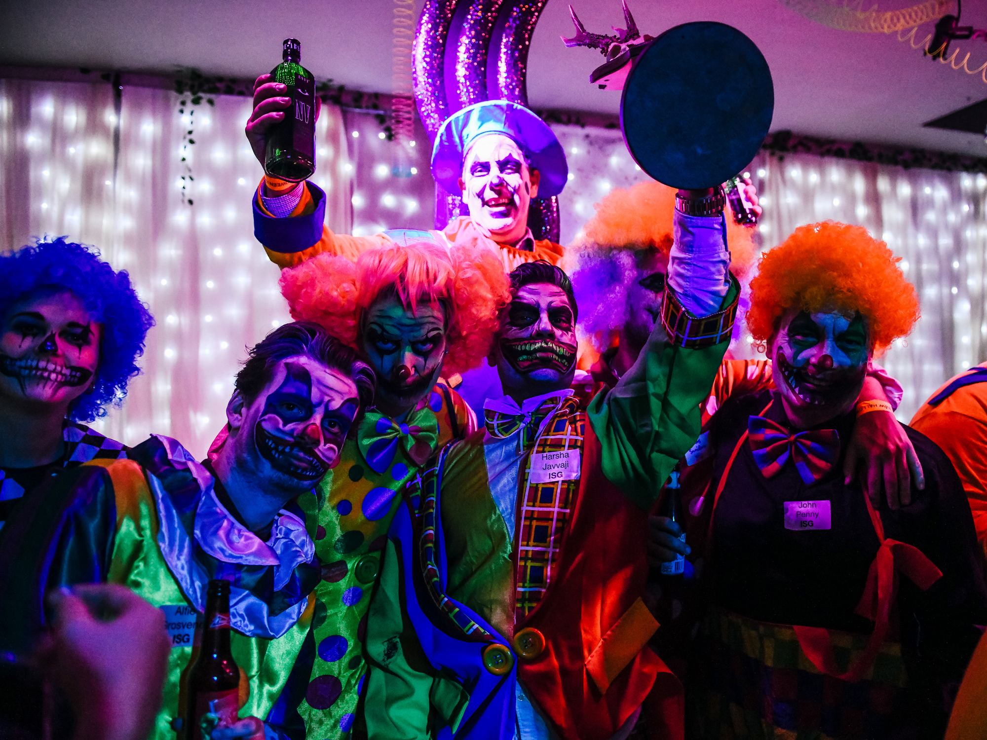 A vibrant group of people in clown costumes and skeleton face paint, celebrating with drinks in a festively lit room.