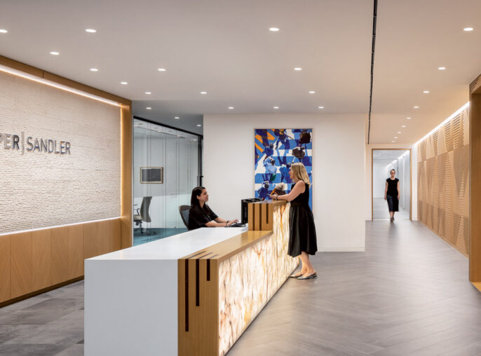 Reception area featuring minimalist design with a sleek, marble desk, warm wooden wall slats, and dynamic chevron-patterned flooring. Recessed lighting accentuates a textured feature wall and contemporary art adds a pop of color.