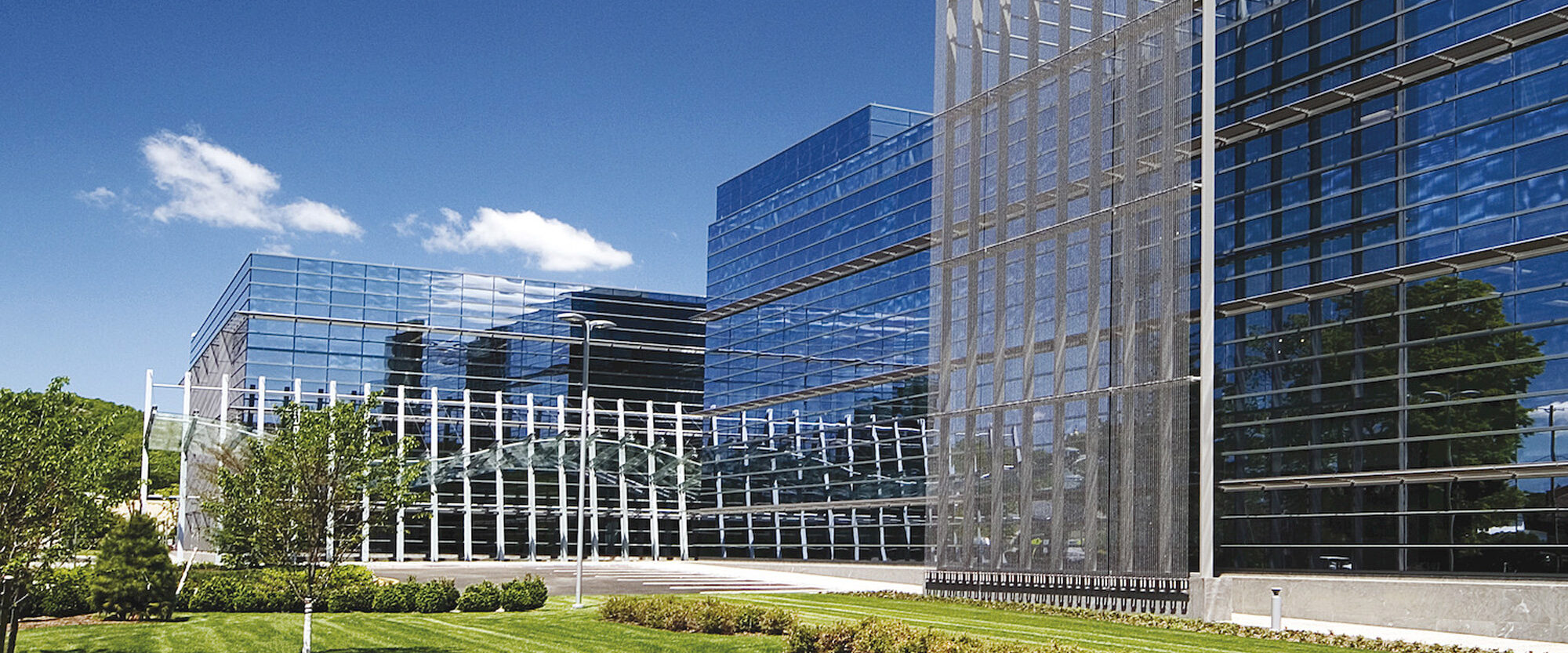 Modern architectural design featuring a commercial building with a reflective glass facade, showcasing a blend of transparent and opaque elements, surrounded by manicured landscaping under a clear blue sky.