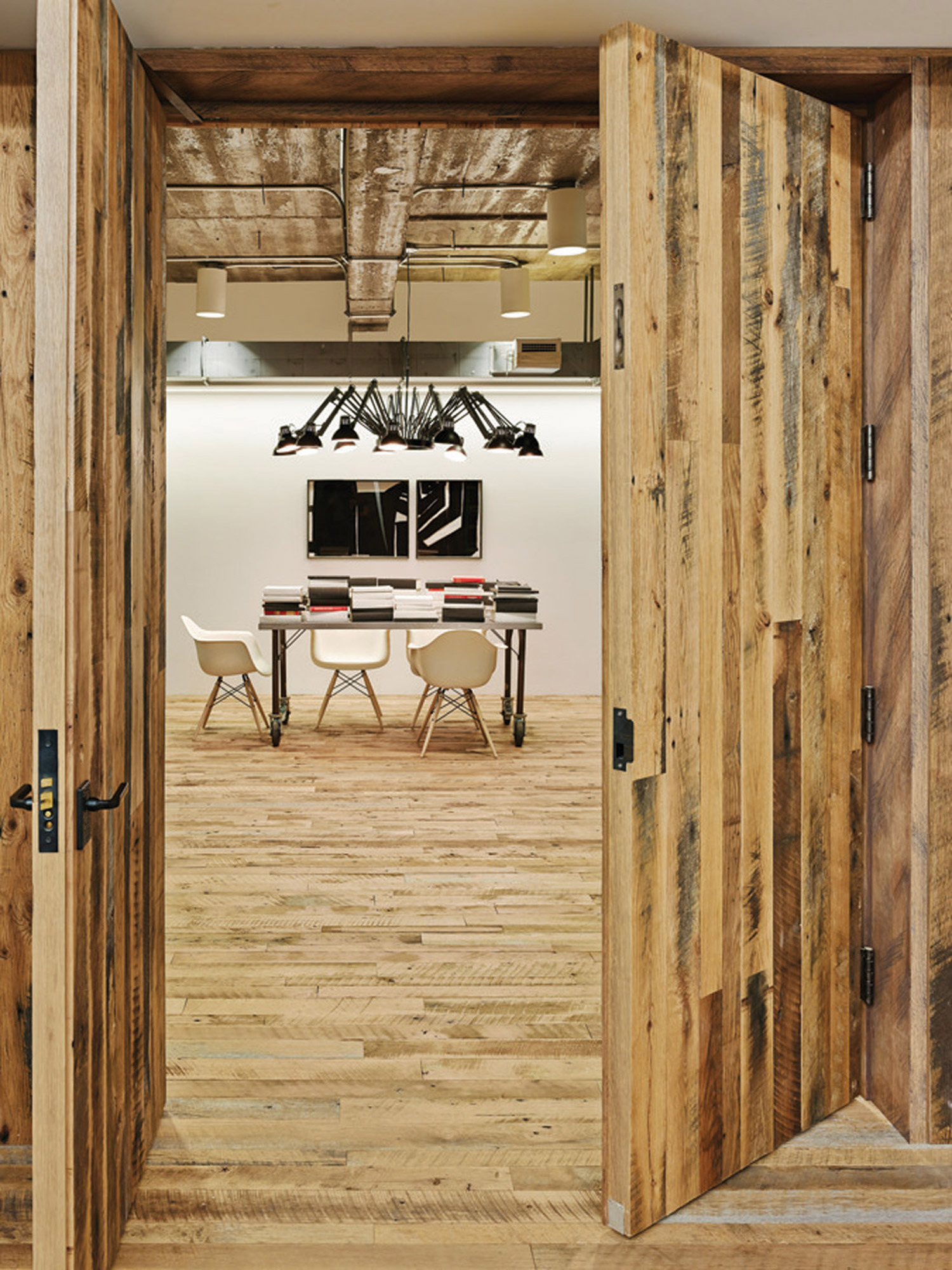 Rustic wooden doors open to a minimalist conference room with sleek chairs and a reflective white tabletop.