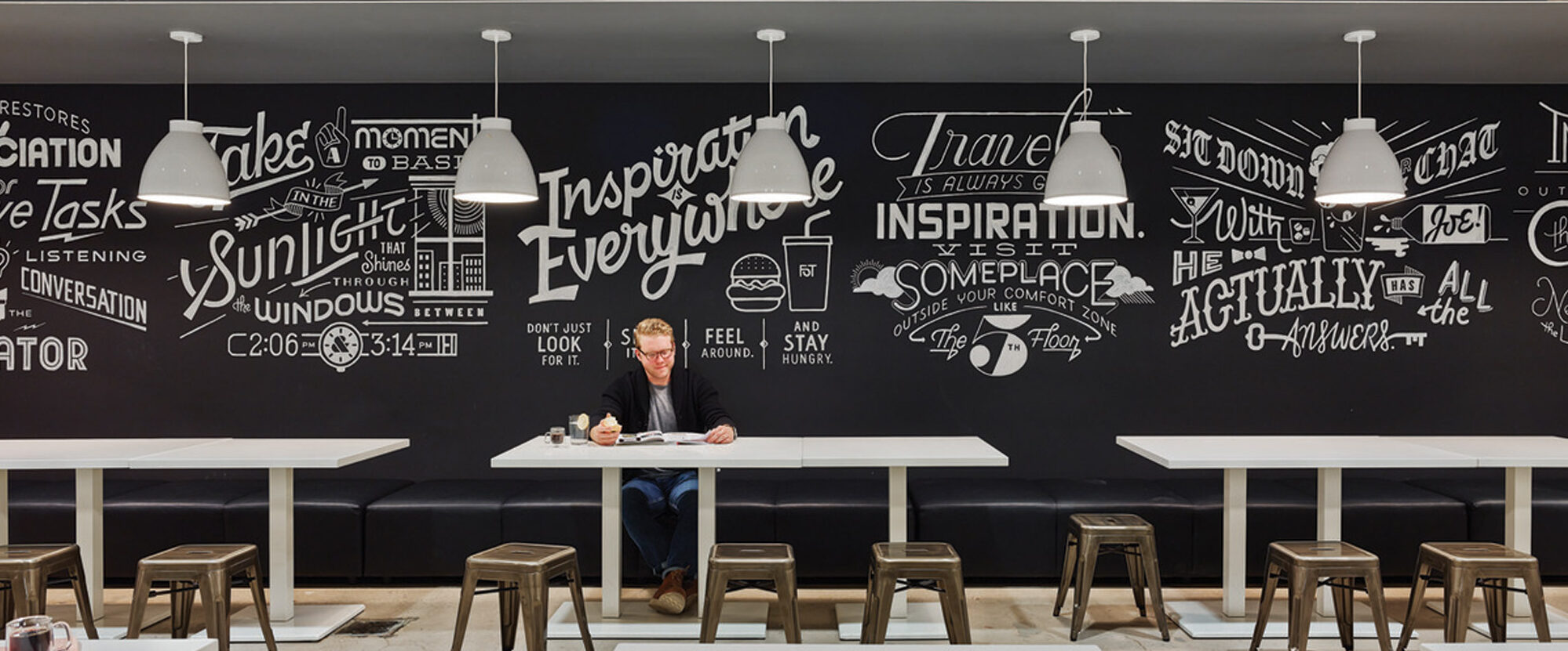 Cafeteria with chalkboard walls filled with creative and inspirational quotes, industrial style lighting, and simple furniture.
