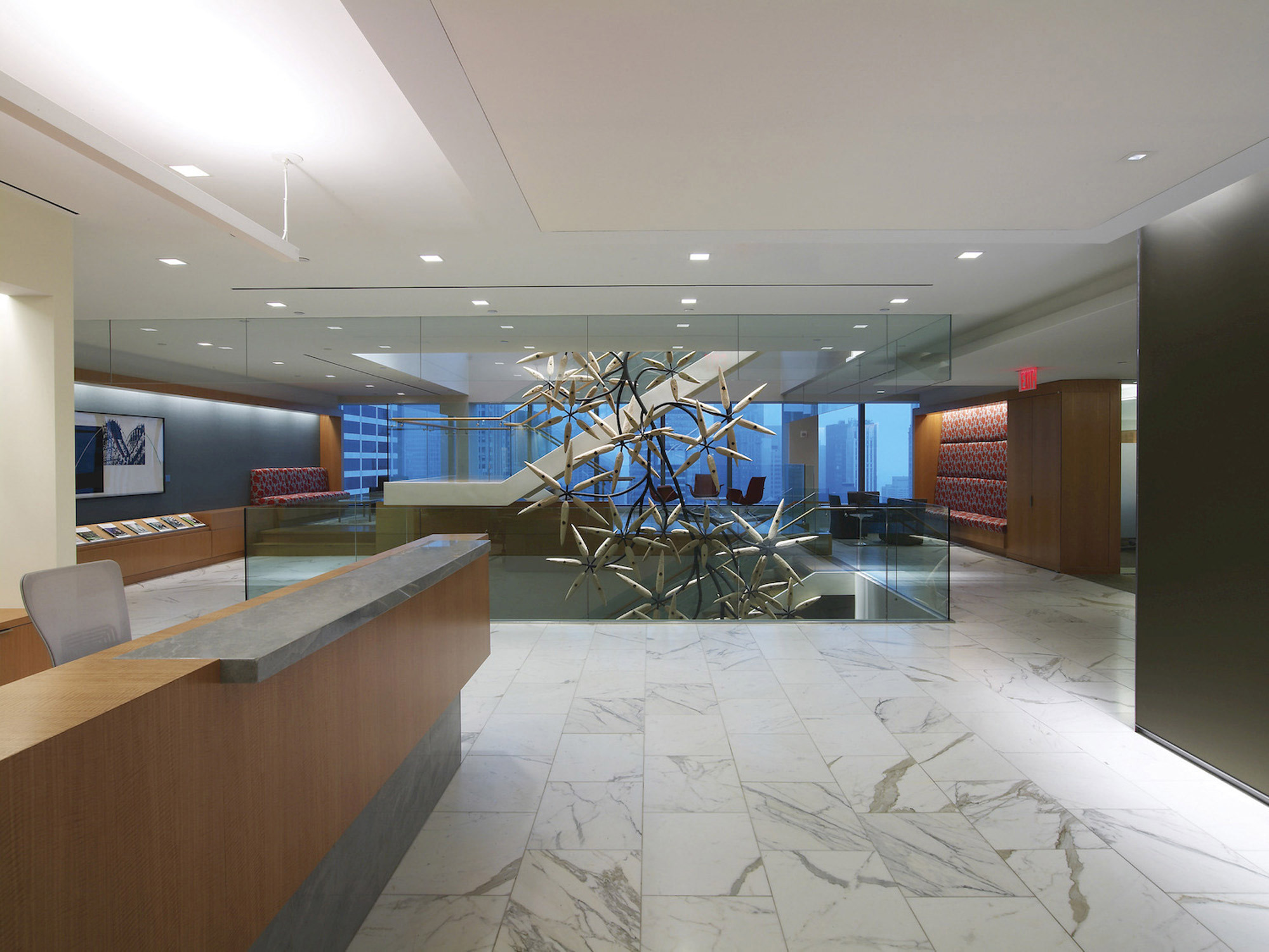 Modern corporate lobby featuring polished marble floors, a geometric central sculpture, sleek glass partitions, and a balanced natural and artificial lighting scheme. Neutral color palette accented with pops of blue on select furniture.