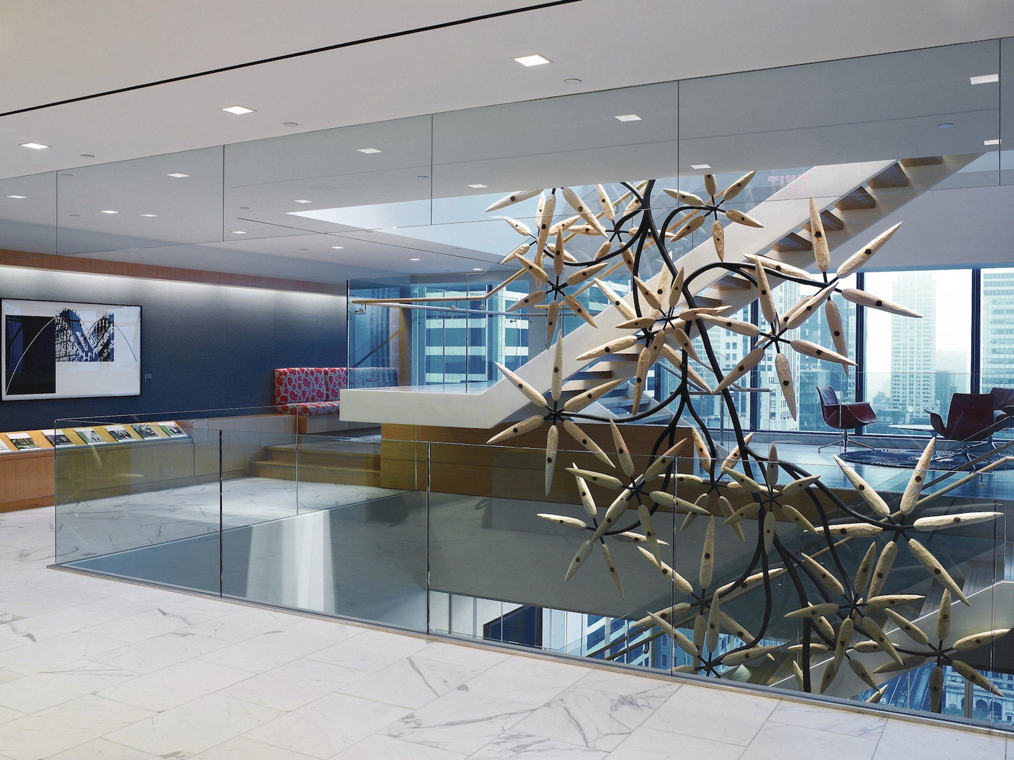 Modern office lobby featuring a geometric wooden sculpture suspended above a glass partition. The space showcases a monochromatic marble floor, minimalist furniture, and expansive city views through floor-to-ceiling windows.