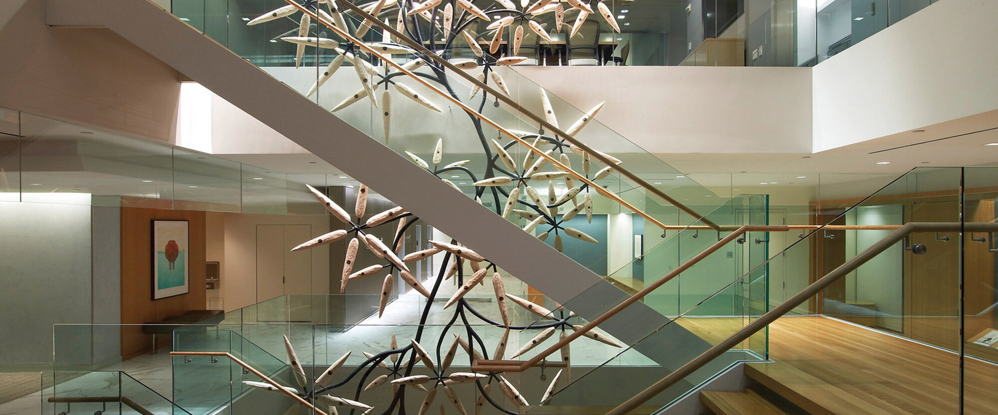 Modern office lobby featuring sleek wood stairs, glass balustrades, and an abstract metallic chandelier evoking a dynamic burst of stars, enhancing the space with a blend of natural materials and contemporary artistry.