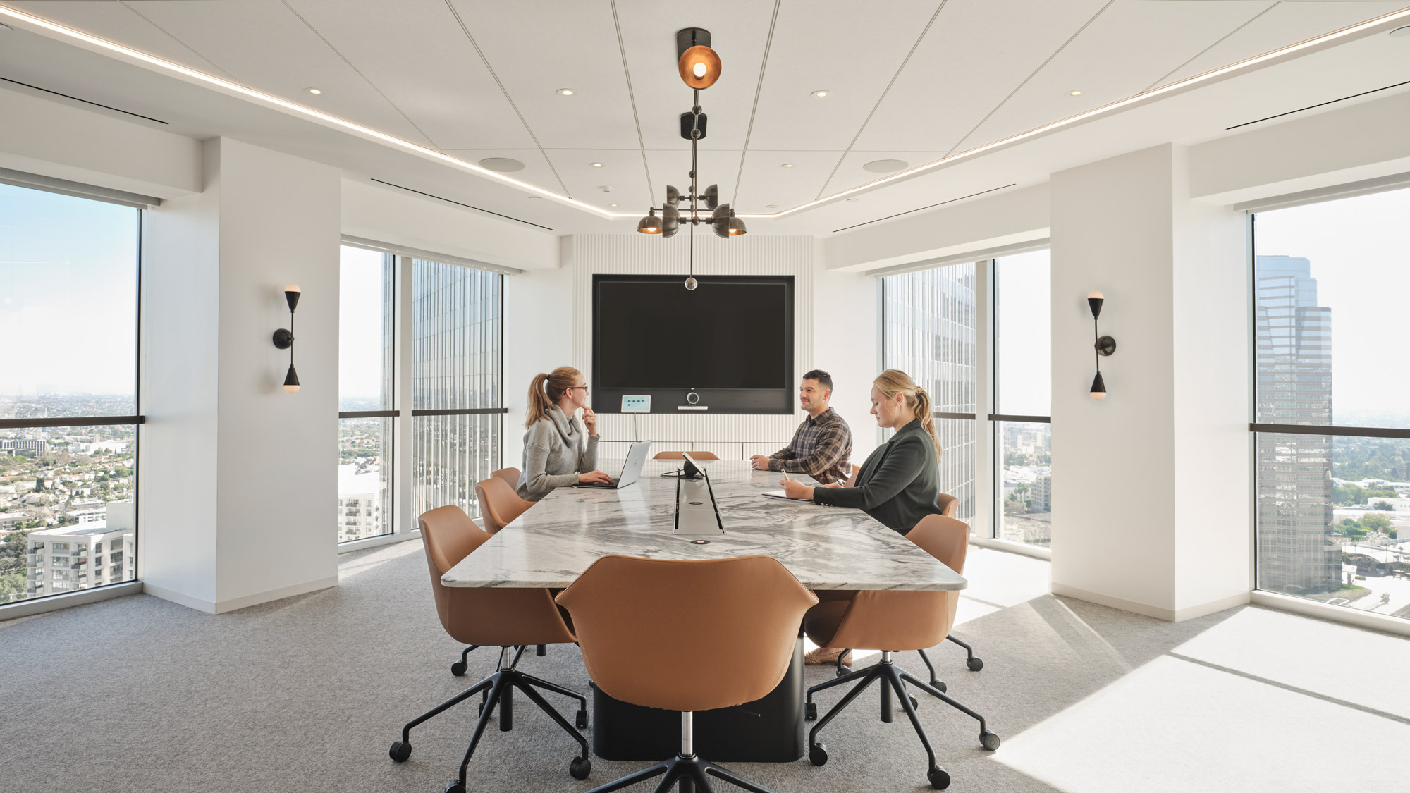 Modern conference room featuring a sleek, oval marble table surrounded by mid-century style chairs, against panoramic windows showcasing city views, complemented by recessed and pendant lighting, with a minimalist aesthetic.