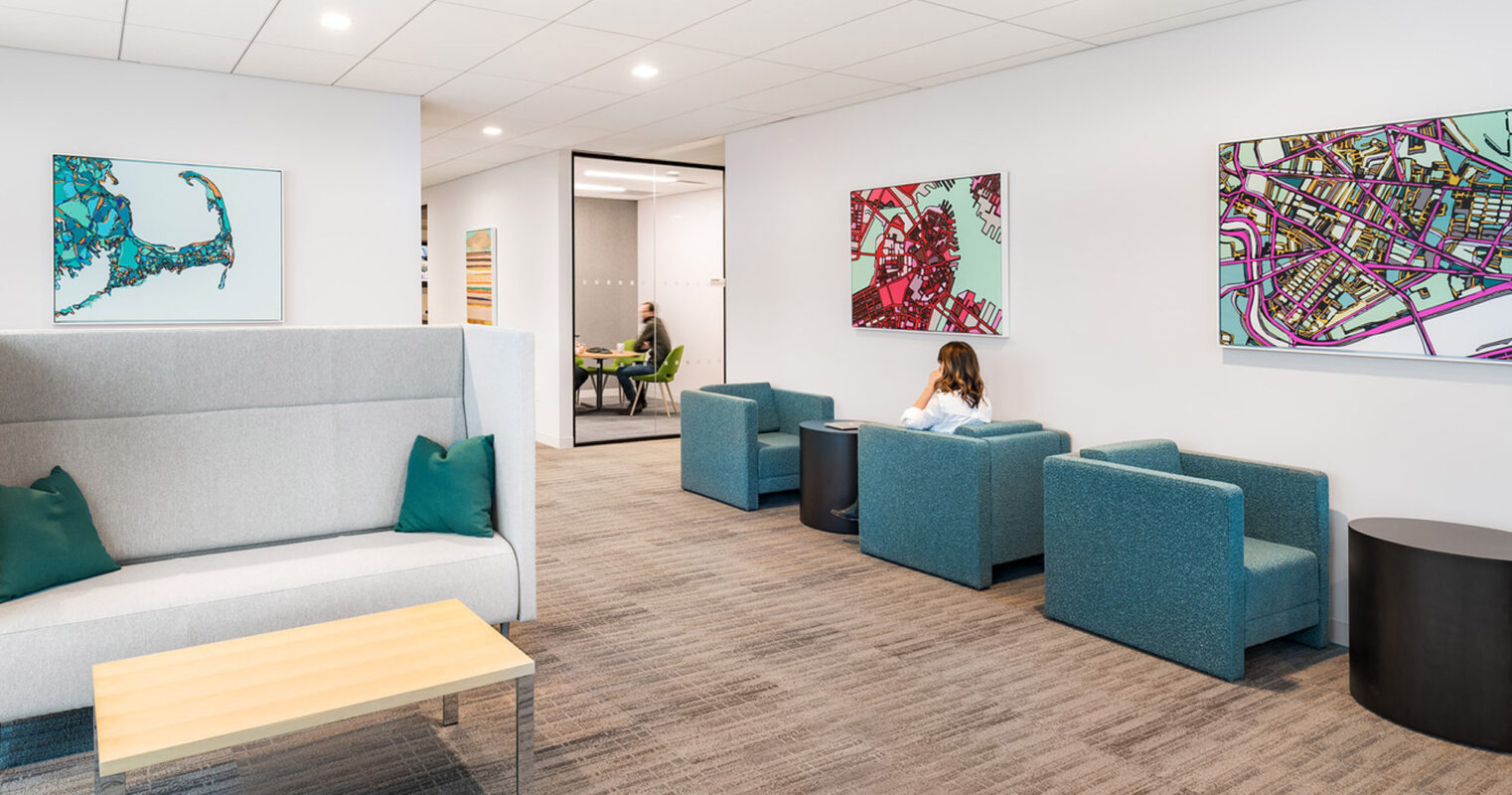 Modern office lounge with clean lines and a neutral color palette complemented by bold artwork. Features include blue upholstered seating, a light wood coffee table, and minimalist decor.