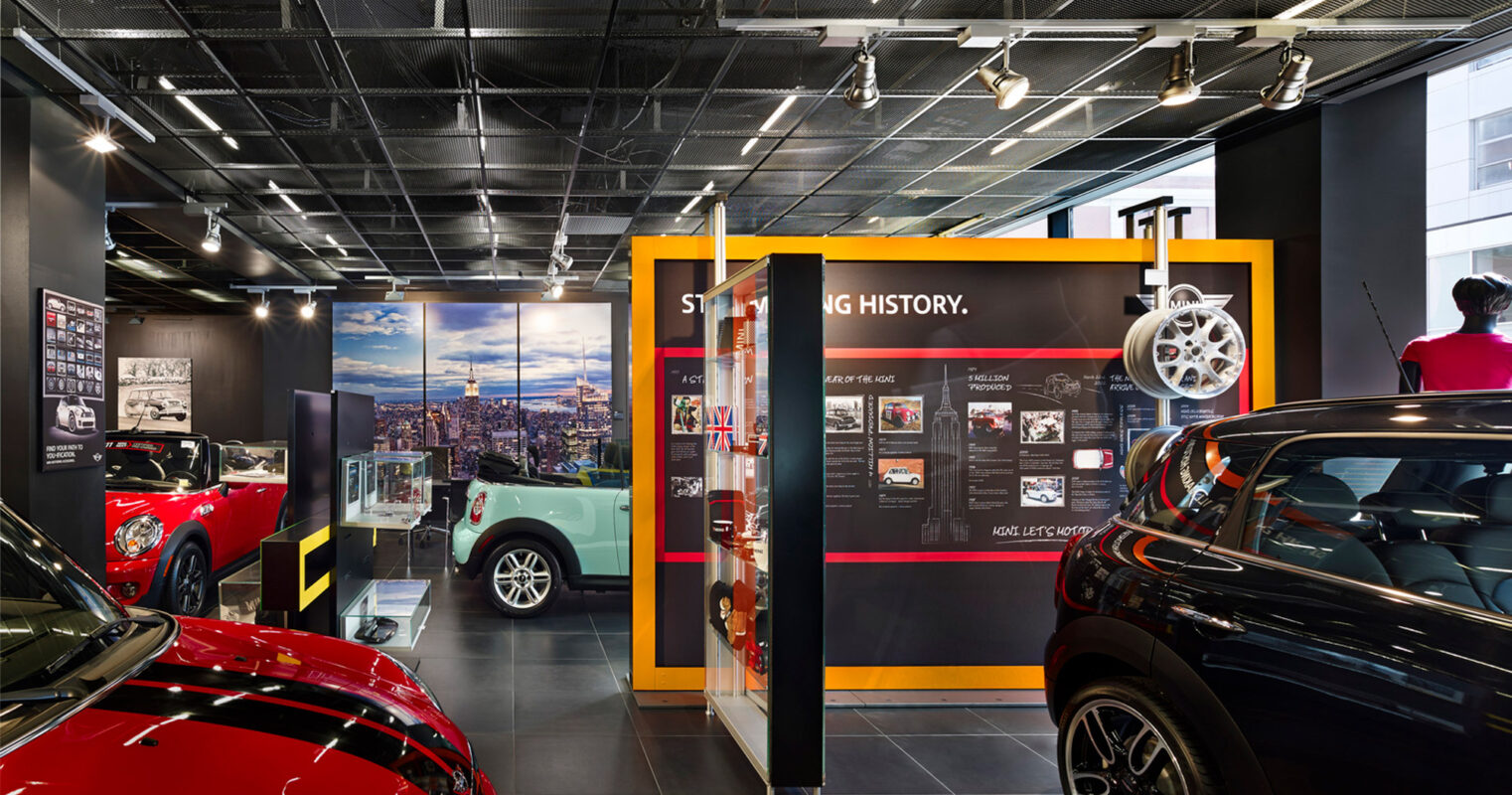 Interior of a car showroom displaying various models, with historical information panels and cityscape imagery.