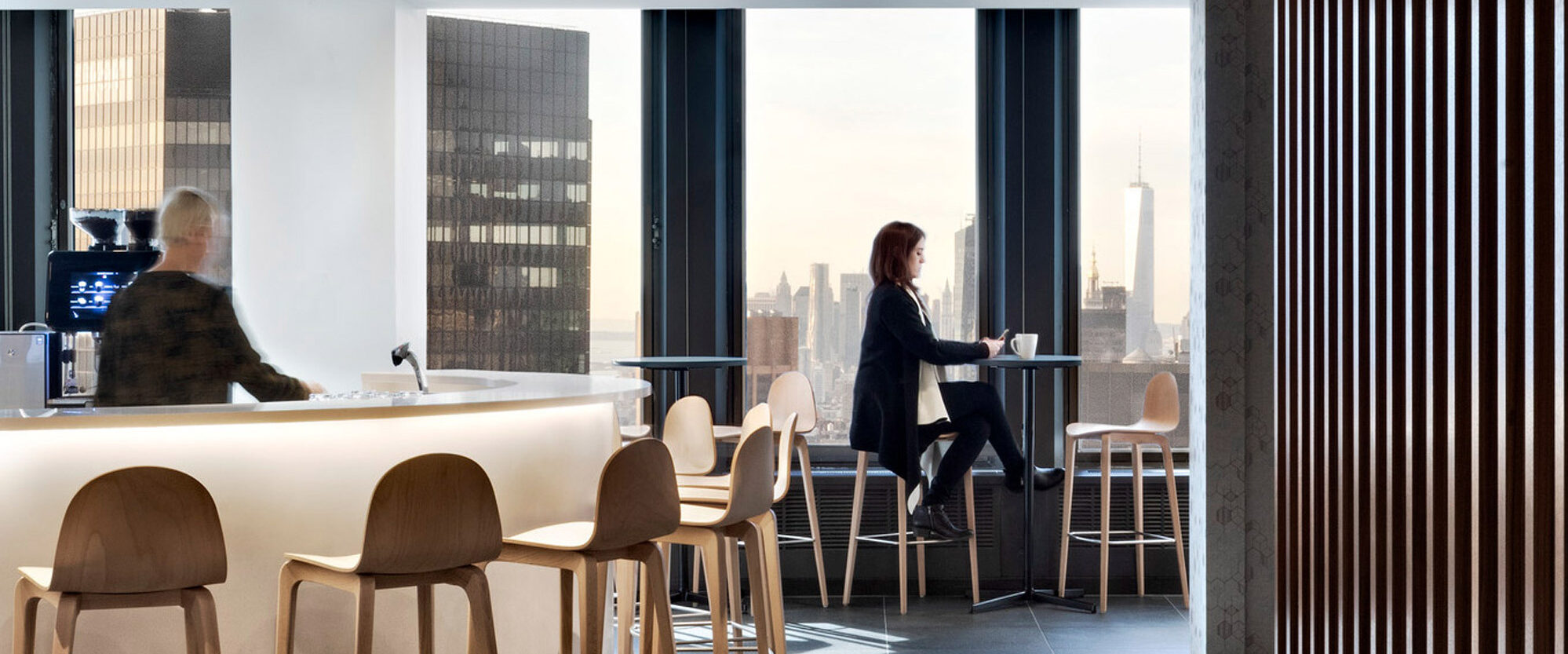 Modern office break area with layered acoustic ceiling, minimalist bar seating, sleek surfaces, and floor-to-ceiling windows revealing a cityscape. Vertical wooden slats provide a textural contrast, enhancing spatial division and visual interest.