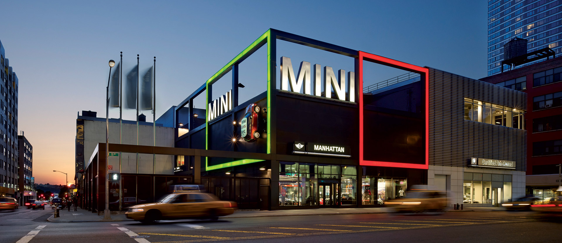 Exterior of a modern car showroom at twilight, featuring vibrant neon-lit framing in green, red, and white, and large glass windows that reveal sleek automobiles and minimalist interior design.