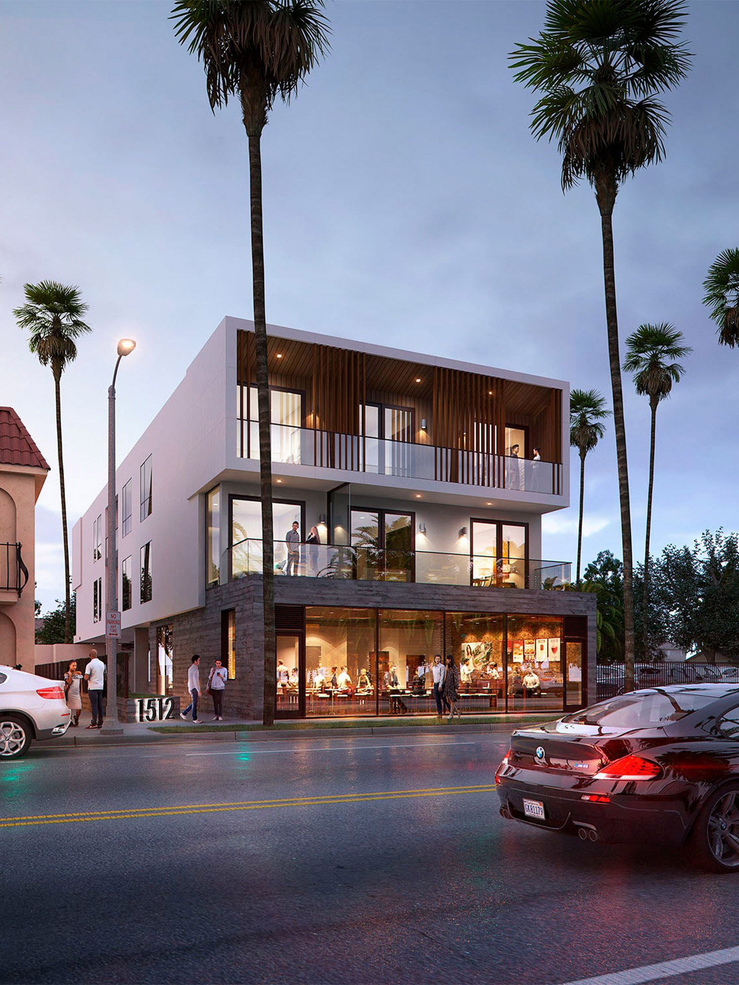 Modern multi-level building at dusk with illuminated interiors, showcasing clean lines and expansive glass windows. Abundant natural light accentuates the open-plan design, which blends commercial spaces on the lower floors with residential balconies above, framed by mature palm trees.