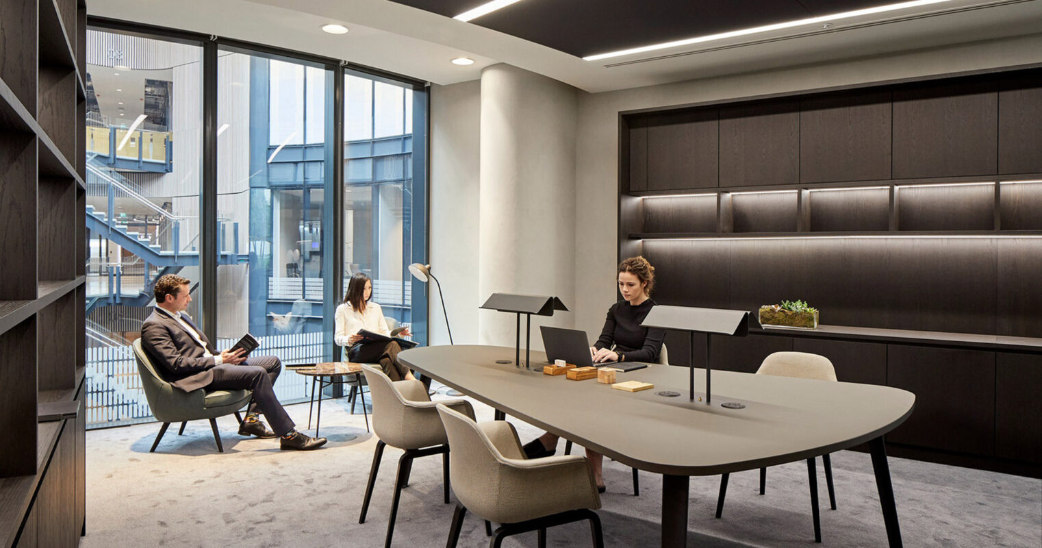 Modern office with ergonomic furniture, accented by a sleek, white kidney-shaped desk, complemented by black upholstered chairs. Ambient lighting highlights the gray textured carpet and panelled walls, creating a dynamic workspace that balances professionalism and contemporary design.