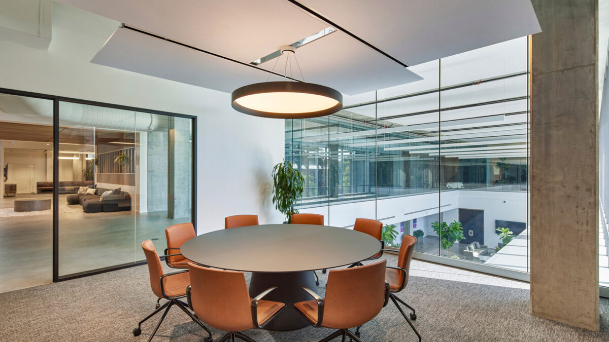 Modern office conference room featuring a round table with terracotta chairs, sleek pendant lighting, floor-to-ceiling glass partitions, and polished concrete flooring, accented by minimalist landscaping. The space employs natural light and clean lines to evoke an air of spaciousness and professionalism.