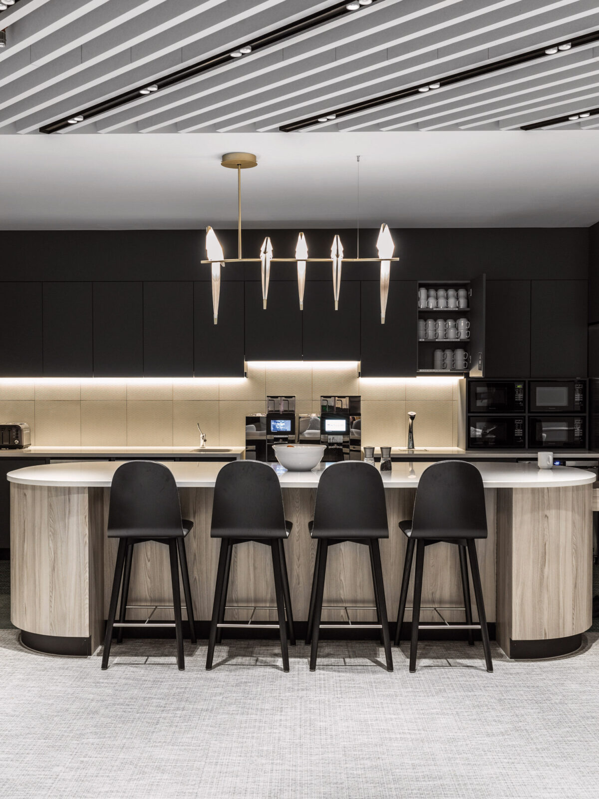 Modern kitchen with curved island, black stools, and pendant lighting. Sleek cabinetry complements the integrated appliances and under-cabinet lighting, showcasing a minimalist aesthetic with a monochrome palette.