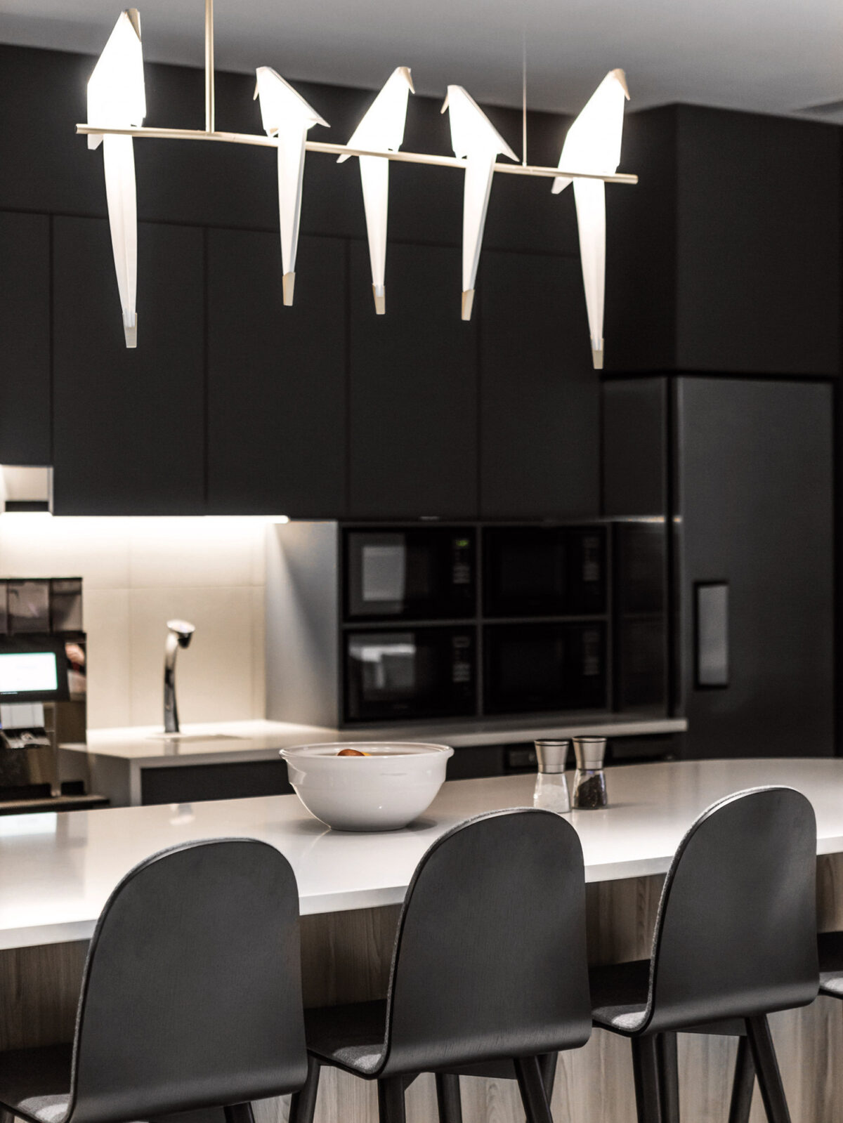 Sleek, modern kitchen with matte black cabinetry and pendant lighting resembling abstract birds in flight above a polished quartz countertop with bar seating.