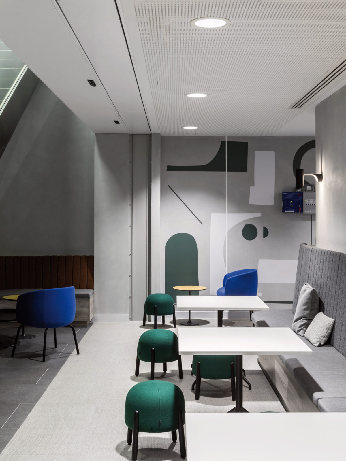 Modern interior space featuring an angular geometric wall mural in muted greens and greys, accented by sleek furniture in contrasting colors, such as blue and green chairs, against a minimalist backdrop. The space combines a play of textures and clean lines, creating a contemporary professional atmosphere.