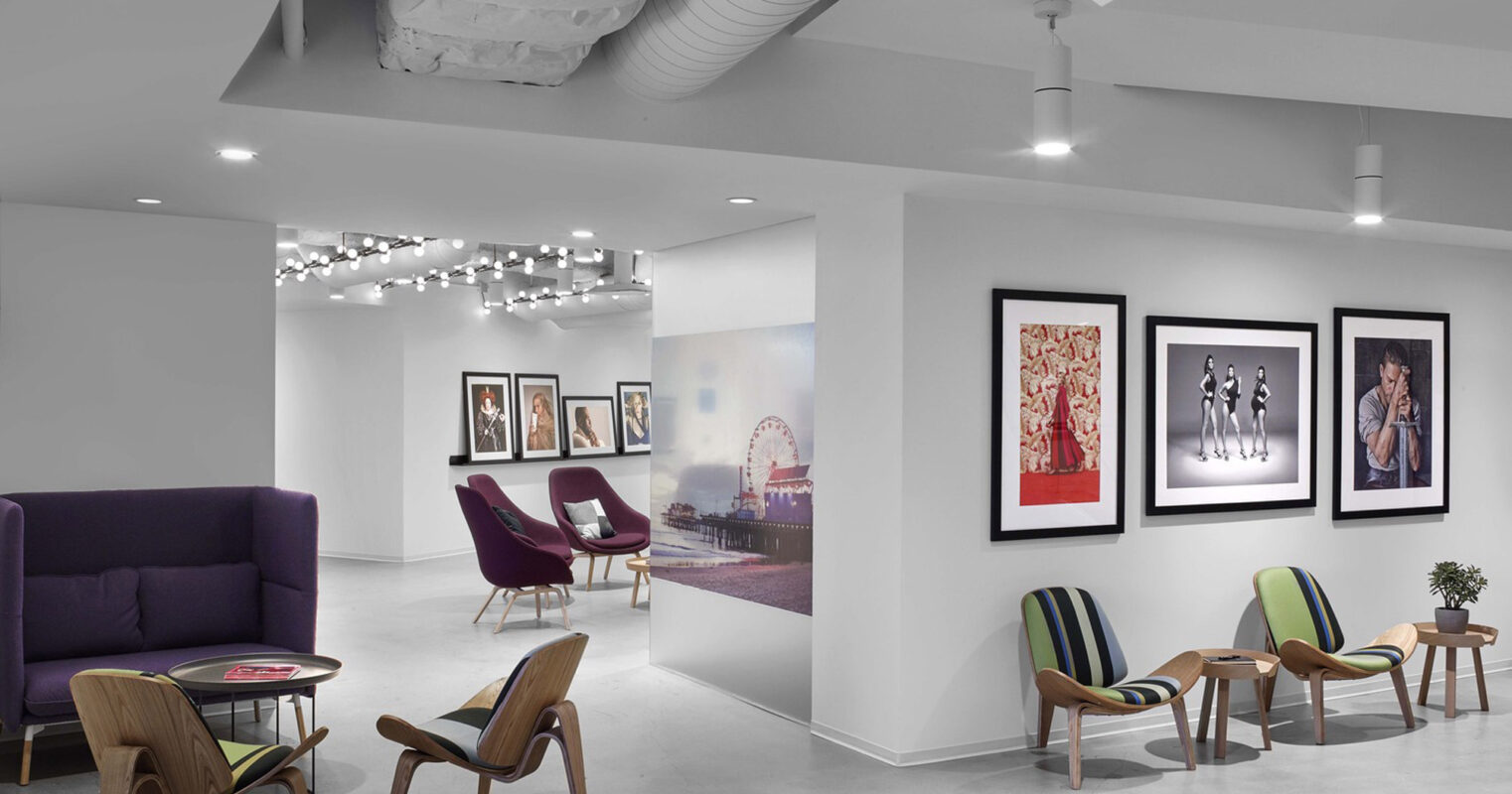 Modern gallery-like interior featuring polished concrete floors, exposed HVAC ductwork on the ceiling, and a mix of vibrant mid-century modern furnishings against a backdrop of bold, framed artwork. A subtle play of textures emerges between the sleek surfaces and soft seating elements.