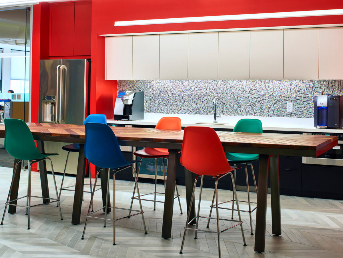 Modern kitchen with vibrant red cabinets above and an island with multicolored chairs. A mosaic backsplash and stainless steel appliances enhance the contemporary design.