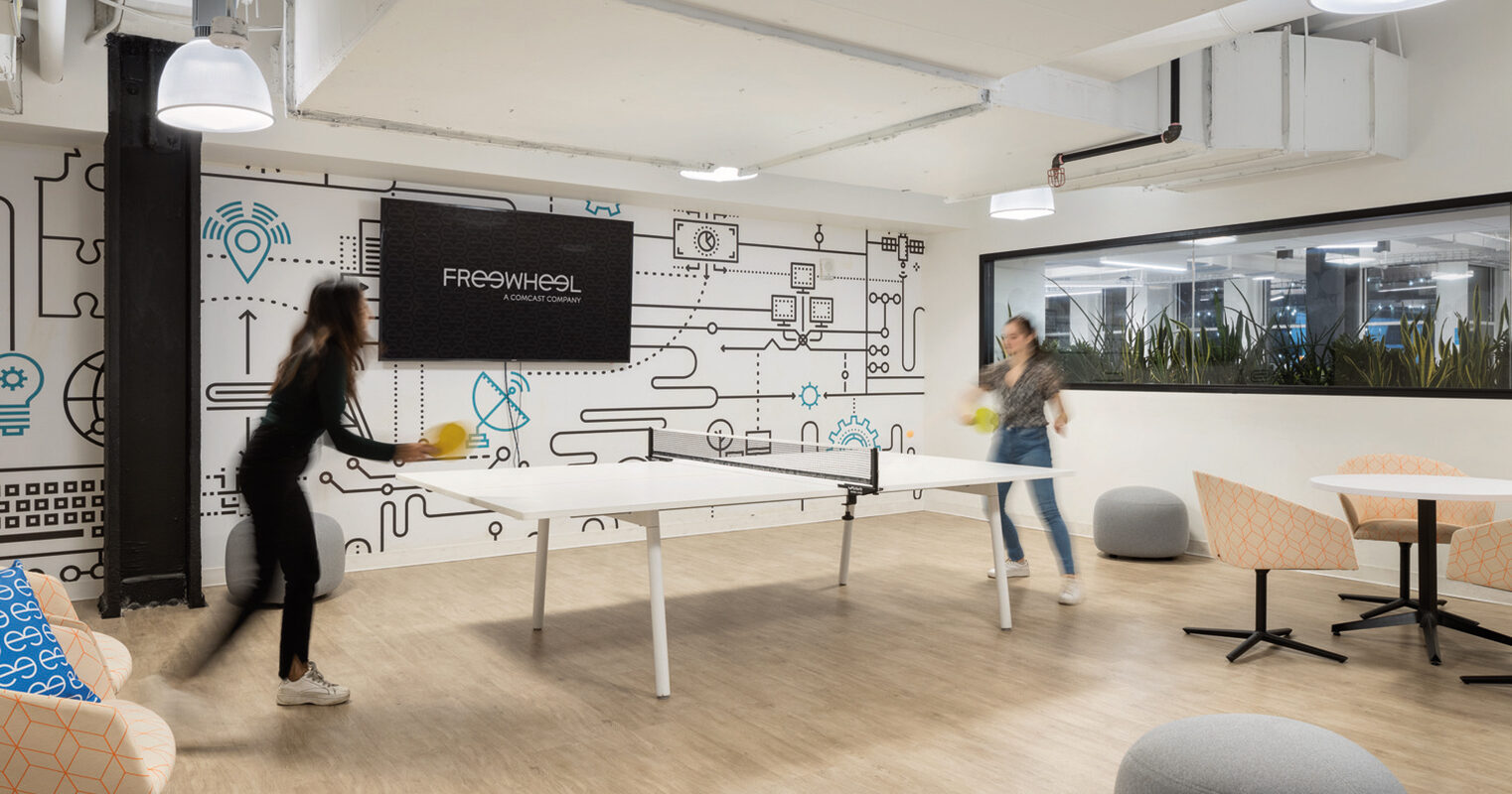 Modern office break room with playful illustrations on accent wall, ping-pong table for recreation, vibrant armchairs, and indoor greenery, integrating leisure with a creative work environment.