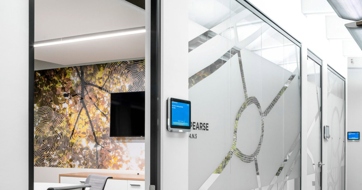 Modern office meeting room featuring a glass partition with abstract frosted design, complemented by an adjacent wall adorned with a vibrant, organic-patterned mural. Overhead, geometric lighting fixtures contribute to a balanced, inviting workspace.