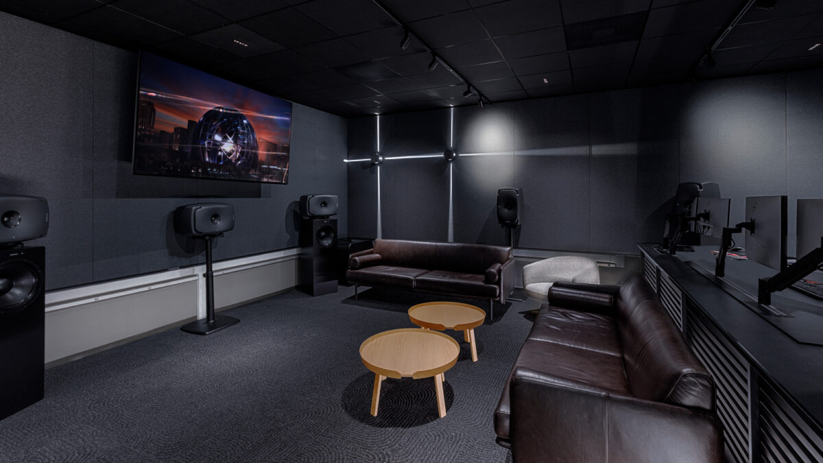 Sleek office theater room featuring a large screen flanked by state-of-the-art speakers, a rich brown leather couch, and complementary modern furnishings against acoustic paneled walls, all designed to enhance the cinematic experience.