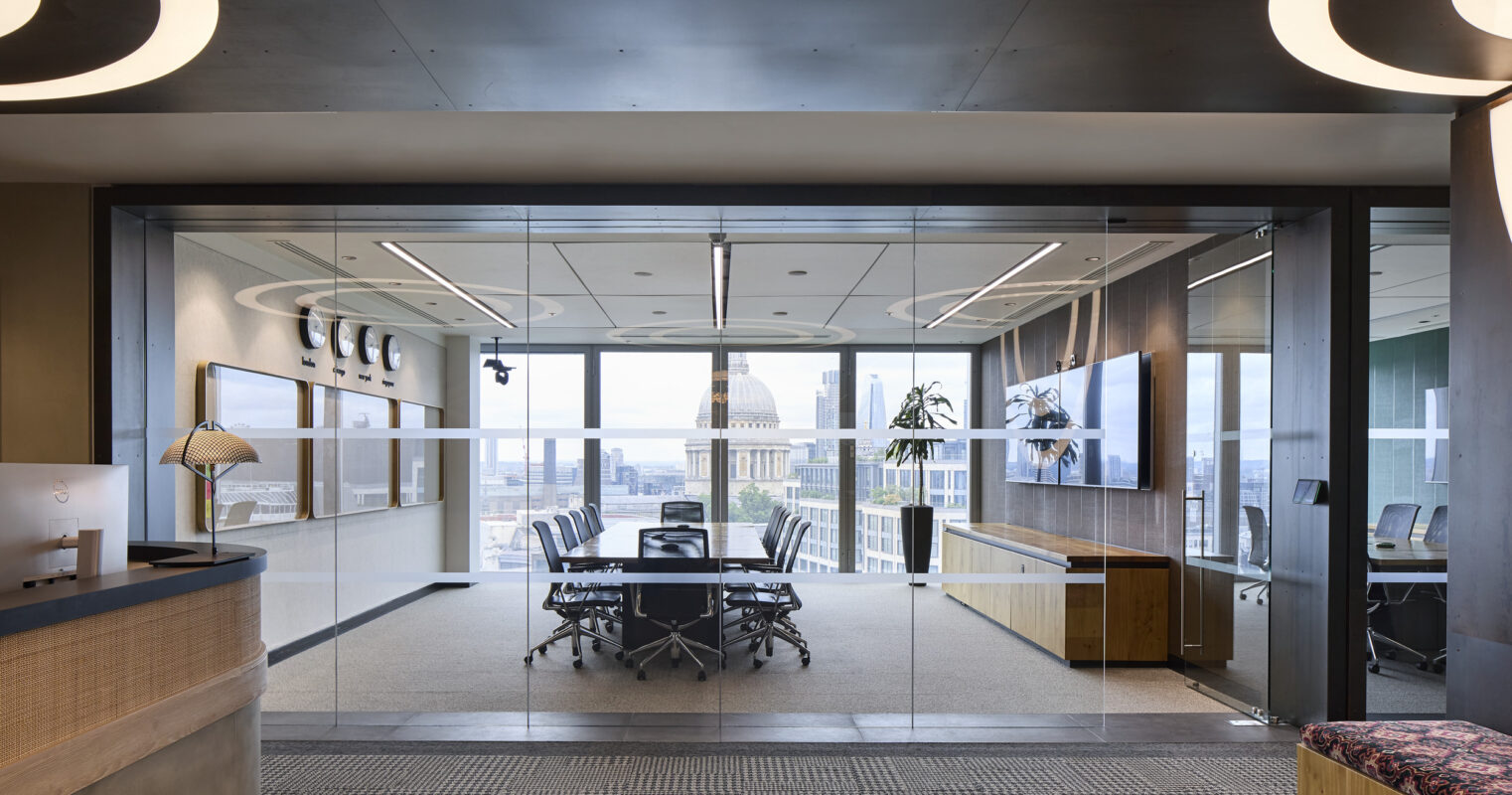 A modern office entrance features a sleek glass doorway leading to a spacious conference room. The interior boasts warm wood accents, contemporary furniture, and sophisticated lighting fixtures, creating a professional yet inviting atmosphere. Large windows offer a panoramic city view, enhancing the workspace's overall ambiance.