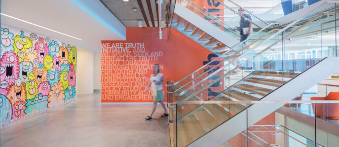 Open-plan office foyer featuring a vibrant graffiti-style mural, polished concrete floors, and a sweeping glass staircase. Exposed ceilings and bold, motivational text enhance the dynamic, creative atmosphere.