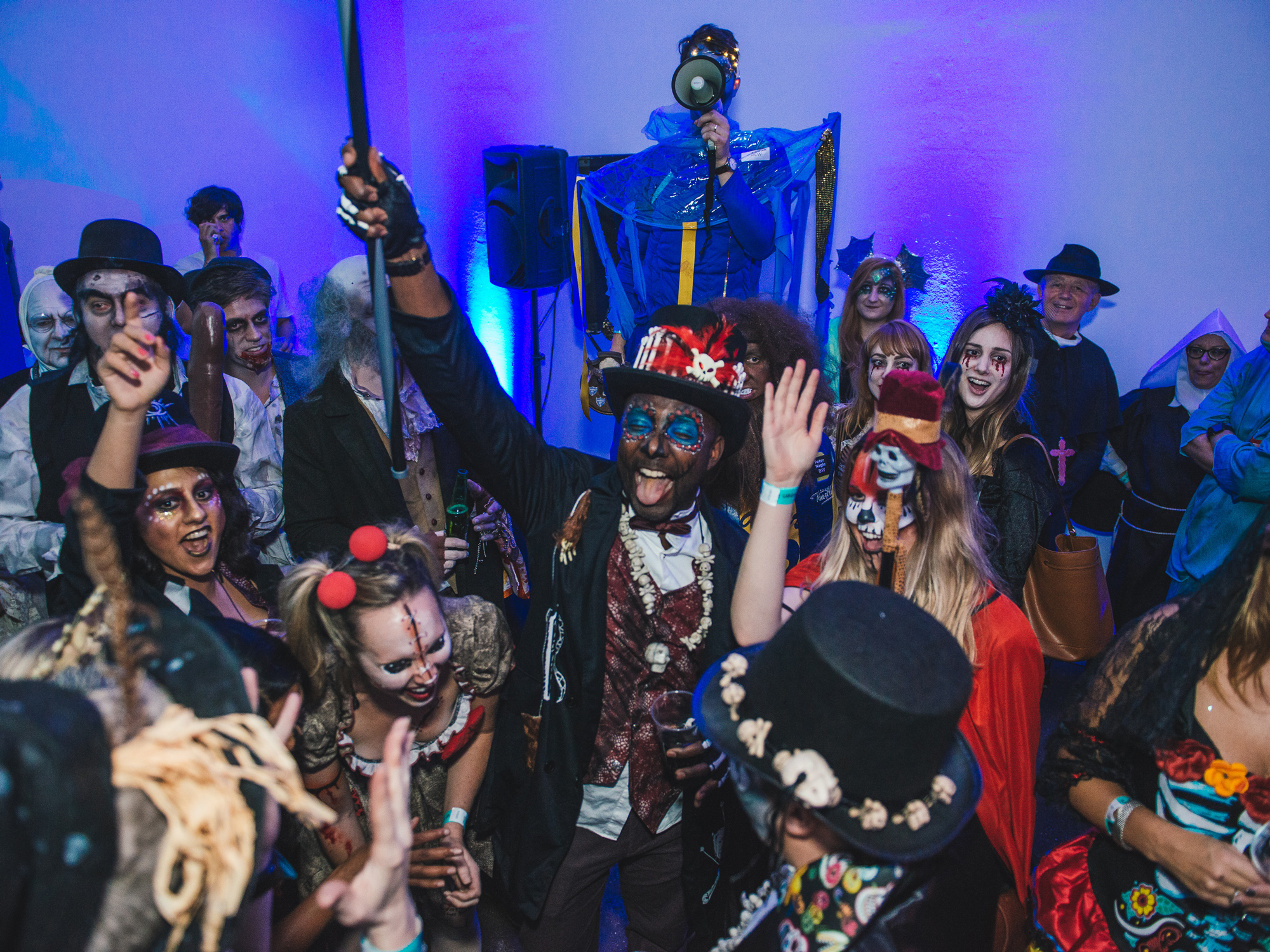 Eclectic mix of party-goers in various horror-themed costumes dancing under a purple light.