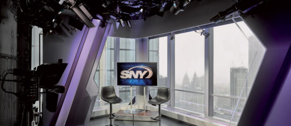 Sleek broadcast studio featuring modern furniture, high-tech lighting, and video equipment with a panoramic window overlooking a cityscape, embodying a contemporary aesthetic.