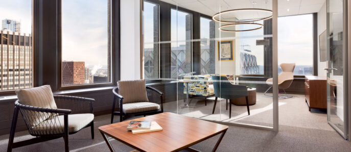 Modern office space with expansive windows offering city views, complemented by geometric furnishings and circular ceiling light fixtures. The neutral palette is accented by a pop of color from wall art and textiles.