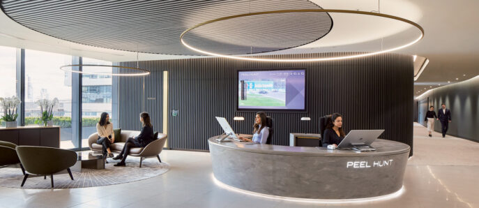Modern corporate lobby with a curved, sleek reception desk, ambient lighting from a circular ceiling feature, and wood-paneled walls. Comfortable seating areas and large screen display enhance the welcoming atmosphere.