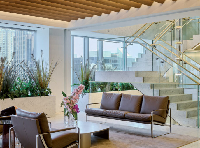 A modern office lobby featuring a recessed ceiling with wooden slats, marble stairs with glass railings, and seating areas with cityscape views.