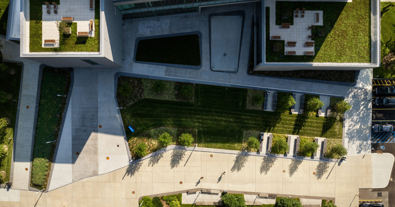 A bird's-eye view of a modern architectural complex with a neatly landscaped courtyard, shadow-casting walkways, and a blend of green spaces and geometric structures. A bird's-eye view of a modern architectural complex with a neatly landscaped courtyard, shadow-casting walkways, and a blend of green spaces and geometric structures. le