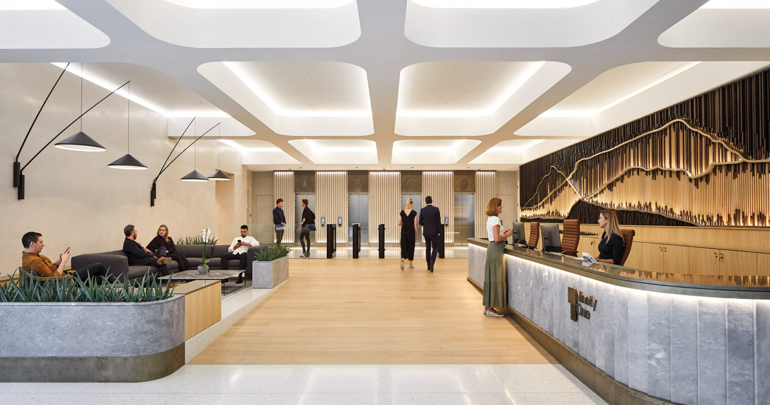 A modern and sleek office lobby with people engaged in various activities, featuring geometric lighting fixtures, wood paneling, and a stylish reception desk.