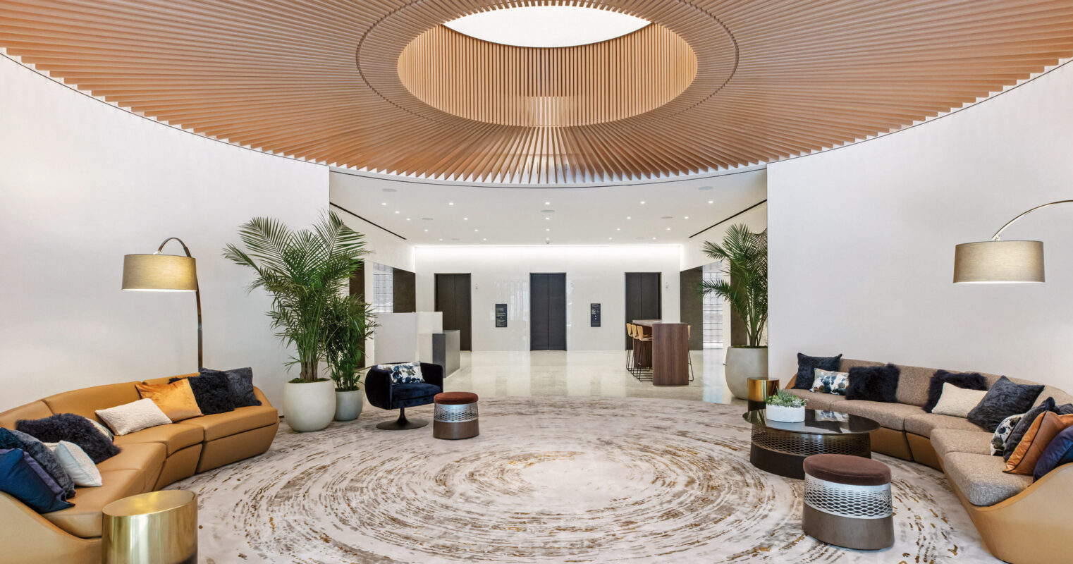 Elegant modern lobby with circular patterned marble floor, wooden slatted ceiling design, and sleek, comfortable seating area complemented by lush indoor plants.