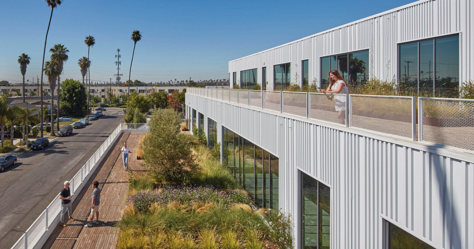 Modern office building integrating green spaces: an employee enjoys a lush rooftop garden walkway, with palm trees and blue skies in the background, emphasizing eco-friendly design and work-life balance.