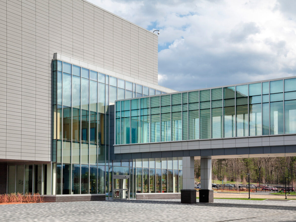 Modern corporate building featuring symmetrical clean lines, extensive use of glass for natural lighting, and a connecting glass-walled skywalk against a dynamic sky backdrop.