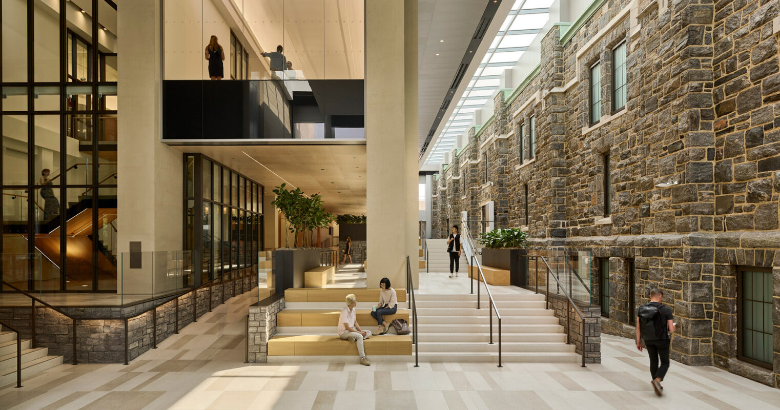 Modern atrium in a renovated building blending contemporary design with historical architecture, where people casually interact and traverse the space.