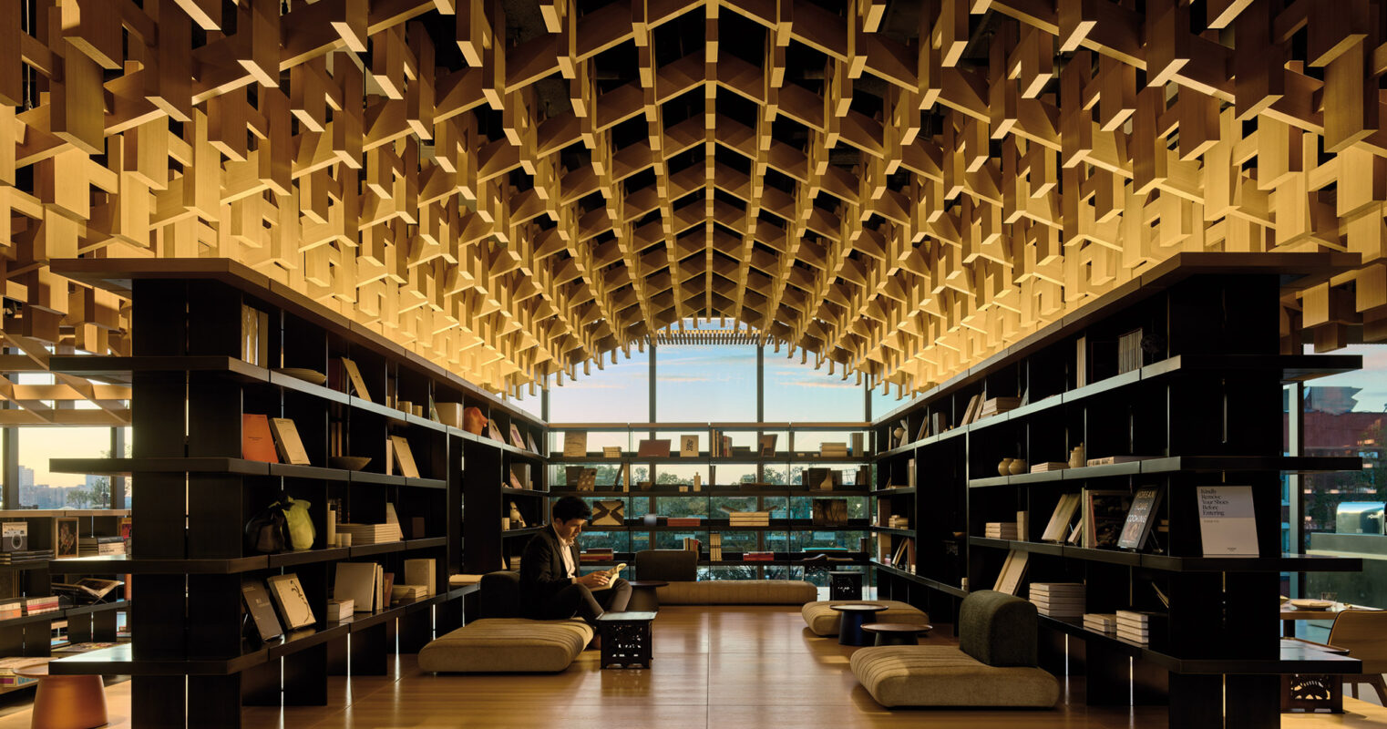 A tranquil and modern library space adorned with an intricate wooden lattice ceiling and cozy seating, inviting visitors to read and explore amidst the geometric harmony.