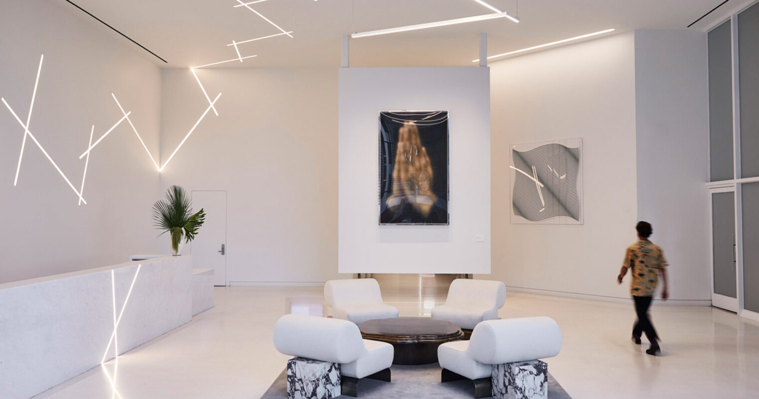 A sleek, modern art gallery space with geometric lighting fixtures, minimalist furniture, and large abstract artworks on the walls, as a person appreciates the art on display.