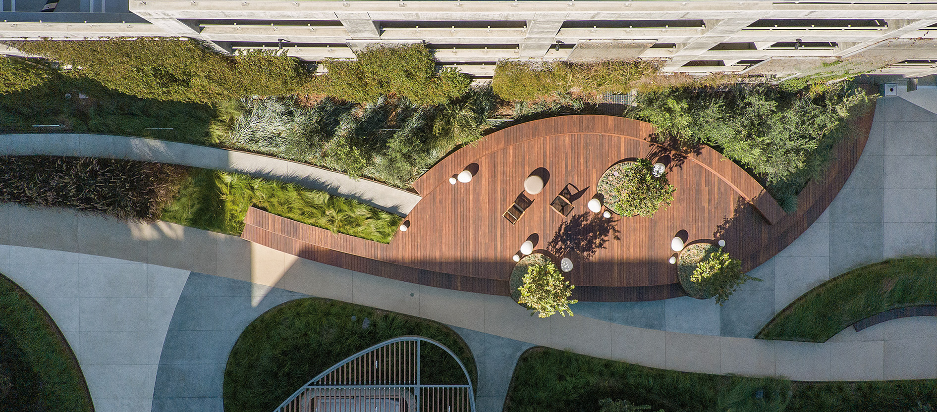 An aerial view of a modern rooftop garden incorporating sleek wooden decking, elegant landscaping, and stylish outdoor seating areas, creating an inviting urban oasis amidst the geometric architecture.