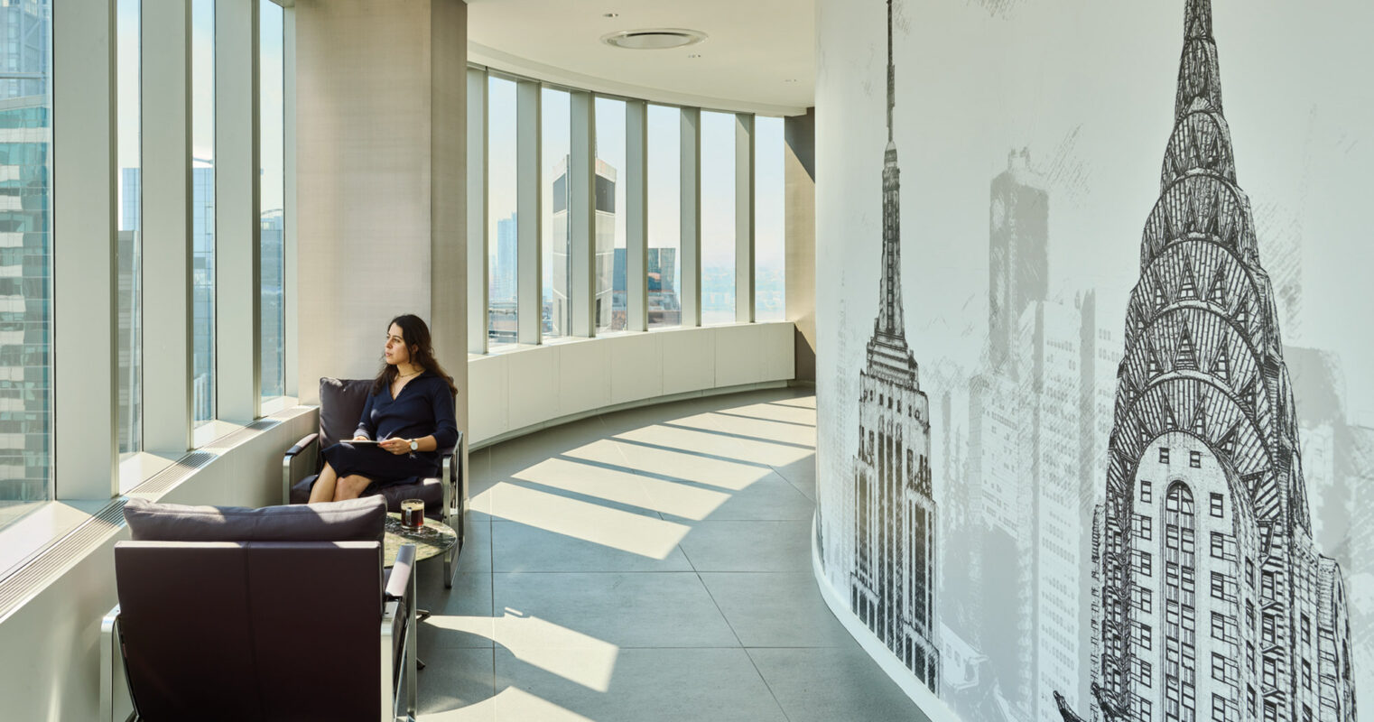 Woman enjoying a moment of contemplation in a modern office with an artistic mural of city skyscrapers on the wall, bathed in natural sunlight from expansive windows overlooking an urban skyline.