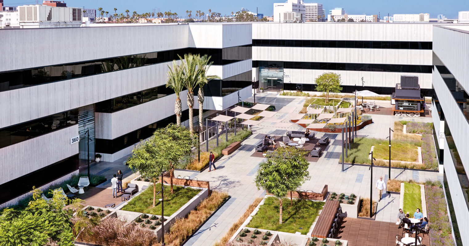 Modern office building with a landscaped outdoor courtyard featuring seating areas, palm trees, and a checkered walkway, encouraging a blend of work and relaxation in an urban setting.