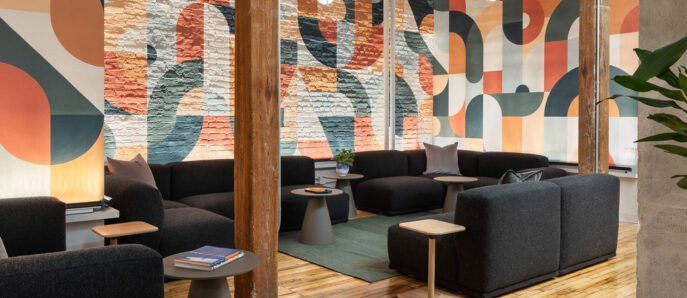 Modern open-plan lounge featuring exposed wooden beams and columns, with a vibrant graphic mural as the backdrop. Earth-tone upholstered modular seating is accented with dark throw pillows, while natural light complements the warm, polished wood floor and planted greenery.