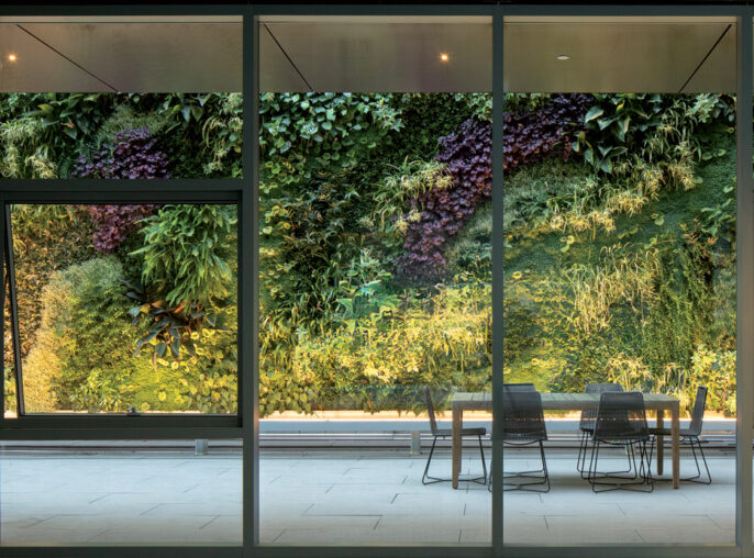 Spacious dining area with floor-to-ceiling glass walls, overlooking a vibrant vertical garden. Sleek furniture contrasts with lush greenery, under soft, ambient lighting for a natural, contemporary atmosphere.