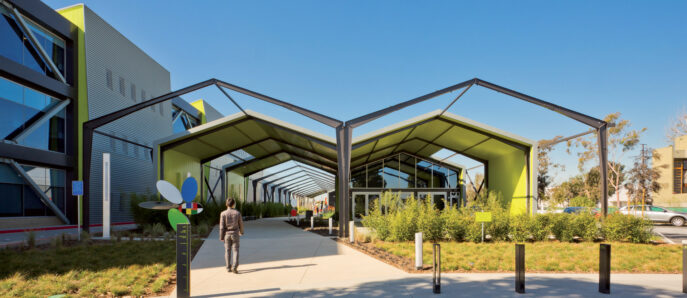 Modern educational facility with a striking geometric canopy entrance, featuring bold yellow accents and angular lines, set against a backdrop of landscaped greenery and contemporarily designed exterior facades.