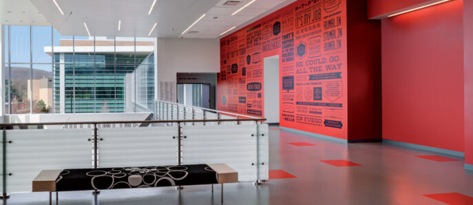 Contemporary office lobby featuring stark white walls contrasted by a vivid red accent wall with typographical artwork, linear lighting fixtures overhead, and minimalistic black furnishings.