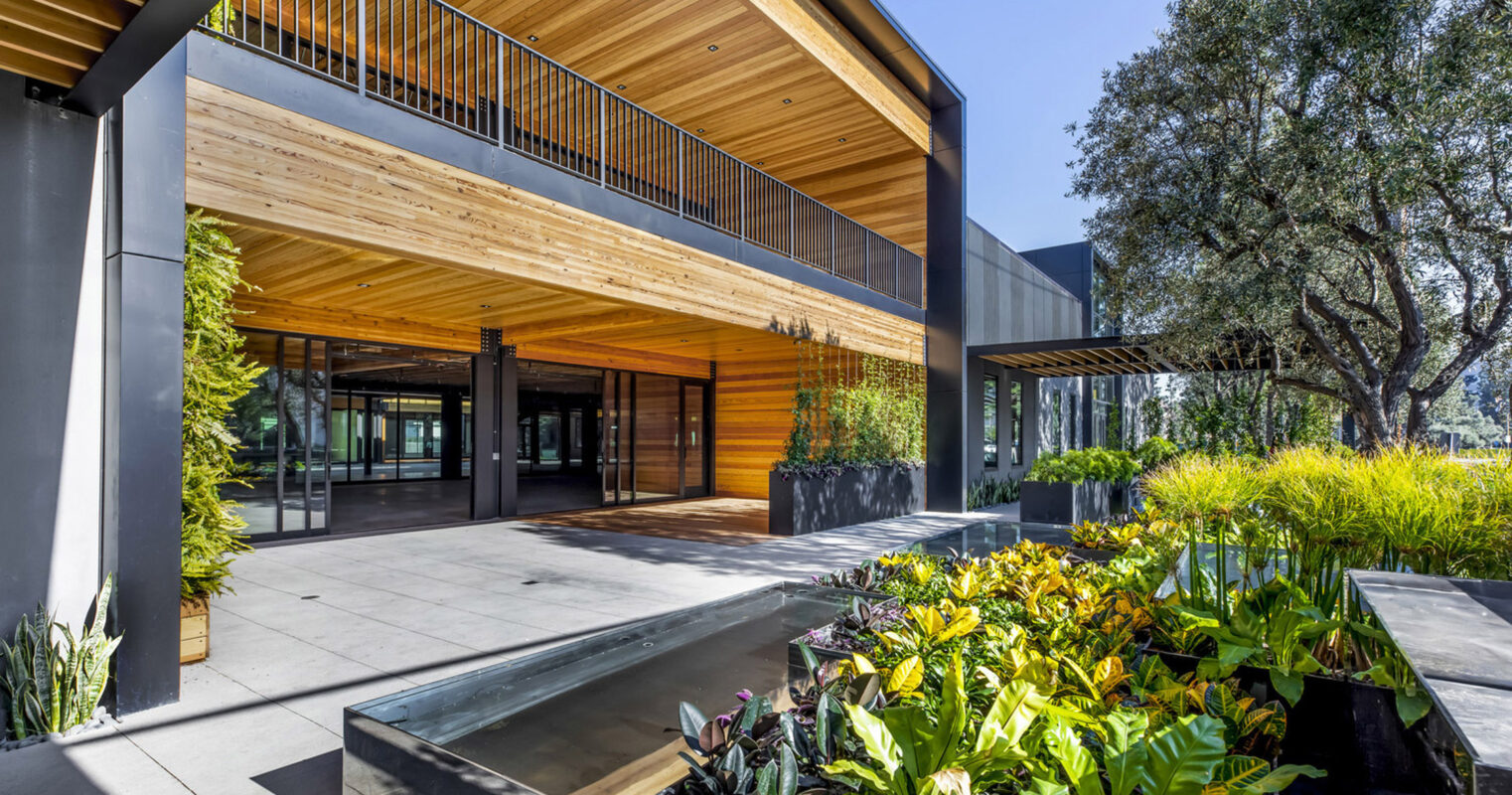 Modern architectural design featuring a building with clean lines, expansive glass windows, and a mix of materials like steel, glass, and natural wood. Landscaped with vibrant greenery and equipped with an accessible entrance.