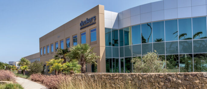 Modern commercial building façade featuring reflective glass windows, beige stucco walls, and landscaped areas with native shrubs and ornamental grasses, showcasing sustainable design principles.